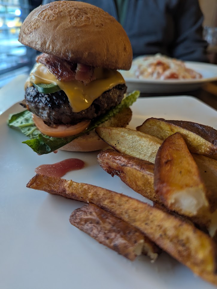 A comically tall 1/2 lb hamburger on a plate with some wedge fries. It's dripping. It's perfect.