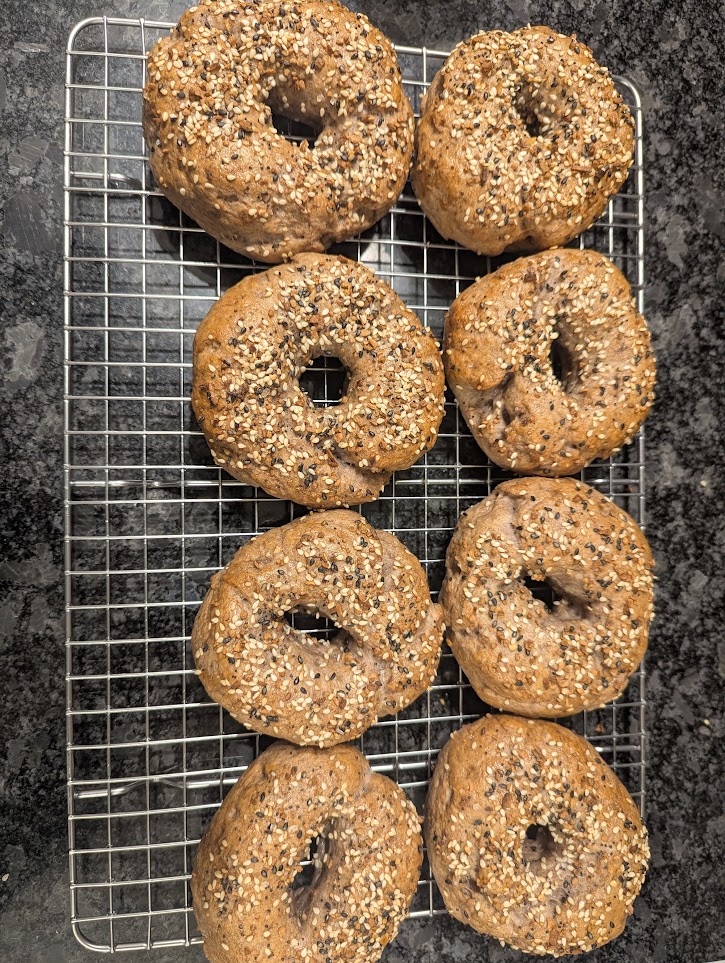 Set of 8 everything bagels cooling on a wire rack on my black countertop.
