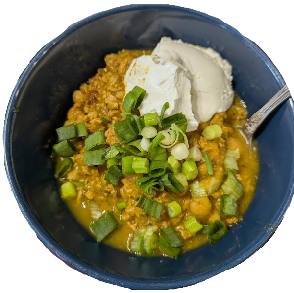 Turkey chili in a dark blue bowl, topped with sour cream and a chopped green onion. The chili is more orange than what you're used to.